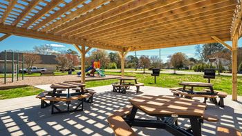 Two picnic tables under a wooden pavilion in a park