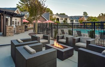 A patio with chairs and a fire pit near a pool