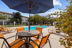 Spokane Valley apartment for rent - A table with chairs and an umbrella is in the foreground of a pool area.