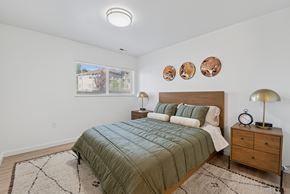 Boise apartment for rent - A bedroom with a bed, nightstand, and a window with a view of a house.