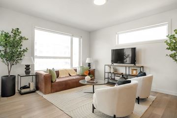 Calgary apartment for rent - A living room with a brown couch, a white chair, and a television on a stand.