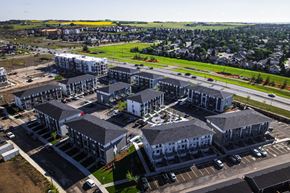 Okotoks apartment for rent - A large, modern building complex with multiple buildings and parking lots.