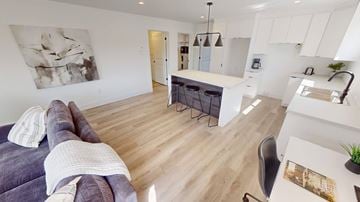 Fredericton apartment for rent - A modern living room with a grey couch and a white kitchen area.