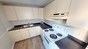 Fredericton apartment for rent - A white stove top oven with four burners is in a kitchen with white cabinets.