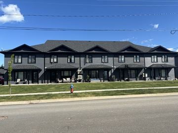 Fredericton apartment for rent - A large grey building with a black roof and a red fire hydrant in front.