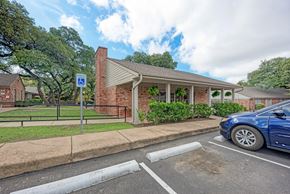 Austin apartment for rent - A blue car is parked in a parking space next to a building with a covered porch.