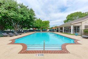 Austin apartment for rent - A large outdoor swimming pool surrounded by trees and lounge chairs.