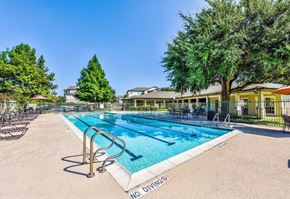 Round Rock apartment for rent - A swimming pool surrounded by trees and a building in the background.