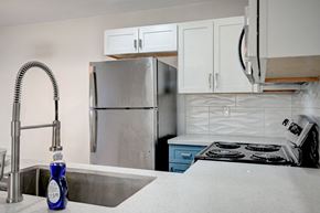 Las Vegas apartment for rent - A kitchen with a stainless steel refrigerator, a sink with a blue bottle on it, and a stove with a white pot on it.