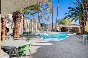 Las Vegas apartment for rent - A pool area with a table and chairs and palm trees.
