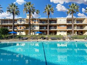 Valley Village apartment for rent - A large swimming pool in front of a multi-story apartment building with palm trees.