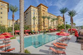Las Vegas apartment for rent - A pool area with red umbrellas and chairs in front of a tan building.