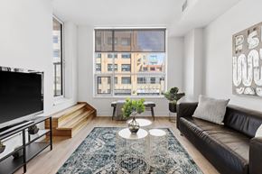 Ottawa apartment for rent - A living room with a black couch, a television, and a large window.