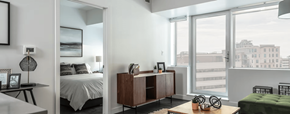 Edmonton apartment for rent - A bedroom with a bed, a nightstand, a chair, and a window overlooking a cityscape.