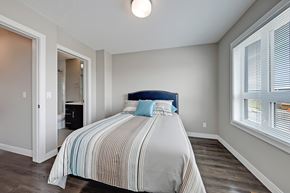 Calgary apartment for rent - A bedroom with a bed, striped comforter, and a window with blinds.