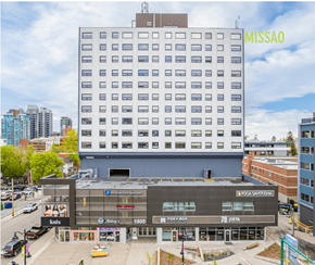 Calgary apartment for rent - A street view of a city with a large building in the background and a smaller building in the foreground with various businesses.