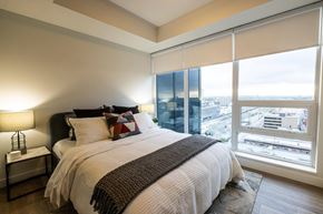 Calgary apartment for rent - A bedroom with a large bed and a city view through the window.