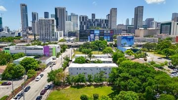 Miami apartment for rent - A cityscape with a mix of modern and older buildings, a road with cars, and a green park area.
