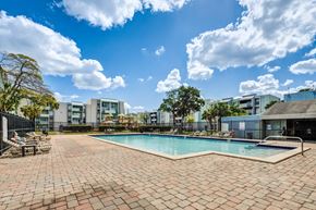 Lauderhill apartment for rent - A swimming pool surrounded by a brick patio and buildings in the background.