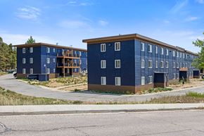 Leadville apartment for rent - A blue building with a brown roof is surrounded by a grassy area and a paved road.