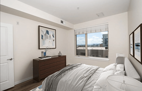 Denver apartment for rent - A bedroom with a bed, nightstand, and a window overlooking a cityscape.