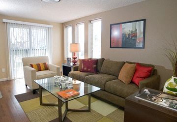 Denver apartment for rent - A living room with a glass table and a couch with a red pillow.