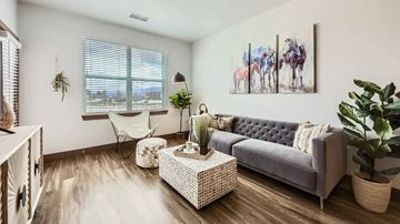 Colorado Springs apartment for rent - A living room with a grey couch, a white wicker coffee table, and a painting of horses on the wall.