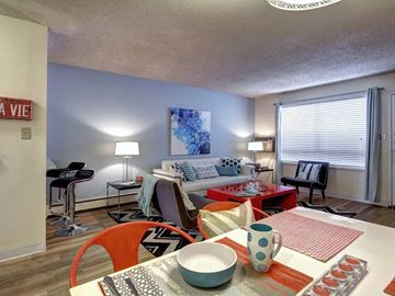 Aurora apartment for rent - A living room with a white couch, a red chair, and a dining table with a bowl and a mug on it.