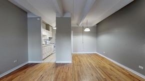 Denver apartment for rent - A room with wooden floors and a kitchen in the background.