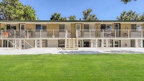 Denver apartment for rent - A 2 story building with white railing and steps leading to each level. Grassy area in front.