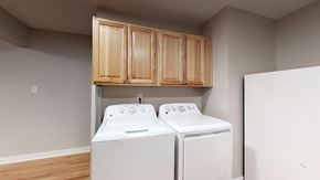 Arvada apartment for rent - A pair of white washing machines are in a laundry room with wooden cabinets above them.