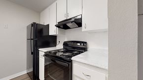 Littleton apartment for rent - A black refrigerator and stove top oven in a kitchen with white cabinets.