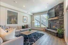 Forest Grove apartment for rent - A modern living room with a grey couch, a fireplace, and a TV mounted on a stone wall at Forestplace Apartment Homes, Forest Grove