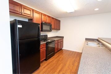 West Lafayette apartment for rent - A black refrigerator is in a kitchen with wooden cabinets and a microwave.
