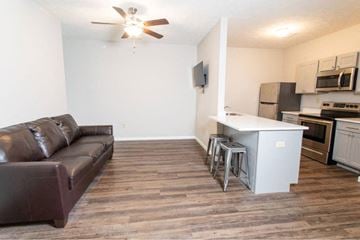 West Lafayette apartment for rent - A brown leather couch sits in a living room with a kitchen in the background.
