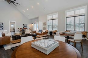 Lewis Center apartment for rent - A large wooden table with a checkerboard in the middle is in the foreground of a spacious room with multiple seating areas and large windows.