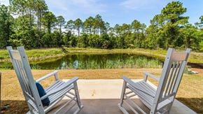 Orange Beach townhouse for rent - Two chairs are placed on a concrete slab with a pond and trees in the background.
