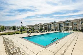 Lake Charles apartment for rent - A large swimming pool surrounded by lounge chairs in front of apartment buildings.
