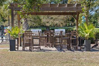 A wooden pergola with chairs and tables is surrounded by greenery