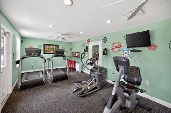 A gym room with treadmills, exercise bikes, and a television.