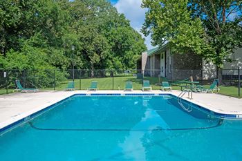 A swimming pool surrounded by trees and chairs.
