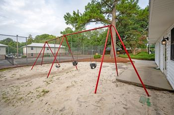 A red swing set sits in a sandy playground.