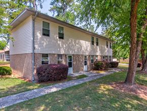 Moncks Corner apartment for rent - A small building with a white door and windows surrounded by greenery at Woodlocke Apartments, Moncks Corner, SC, 27461