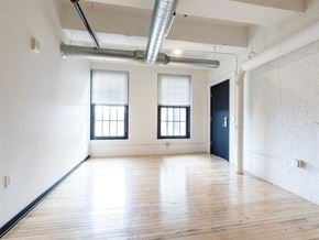Racine apartment for rent - A room with wooden floors and white walls, with two windows and a door on the right side.
