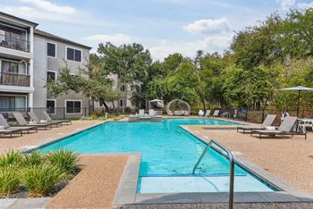 A swimming pool surrounded by lounge chairs and trees.