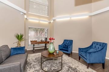 Fort Worth apartment for rent - A living room with a grey couch, a blue armchair, and a coffee table with a green vase on it.