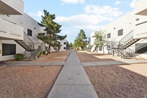 Las Vegas apartment for rent - A long concrete walkway separates two rows of white buildings with trees in between.