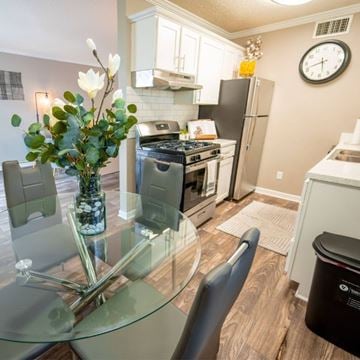 Waco apartment for rent - A kitchen with a glass table and chairs, a vase with flowers, and a clock on the wall.