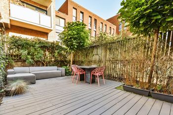 A wooden deck with a table and chairs in the middle of a backyard