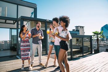Four people are standing on a wooden deck, enjoying drinks and conversation